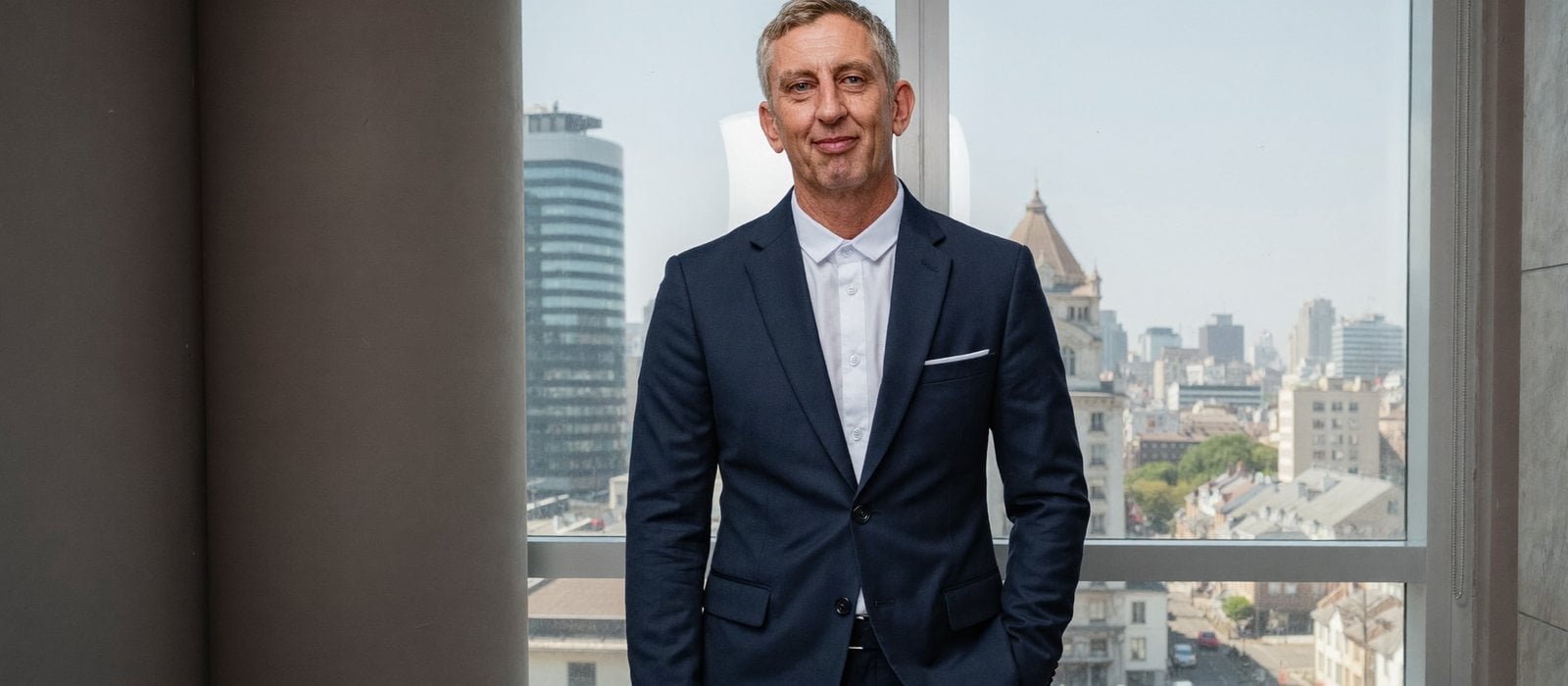 Nick Hall photographed beside a window overlooking a city skyline